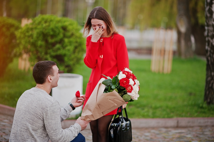 Marriage proposal. Man with boquet of flowers kneeling and give engagement ring for his girlfriend